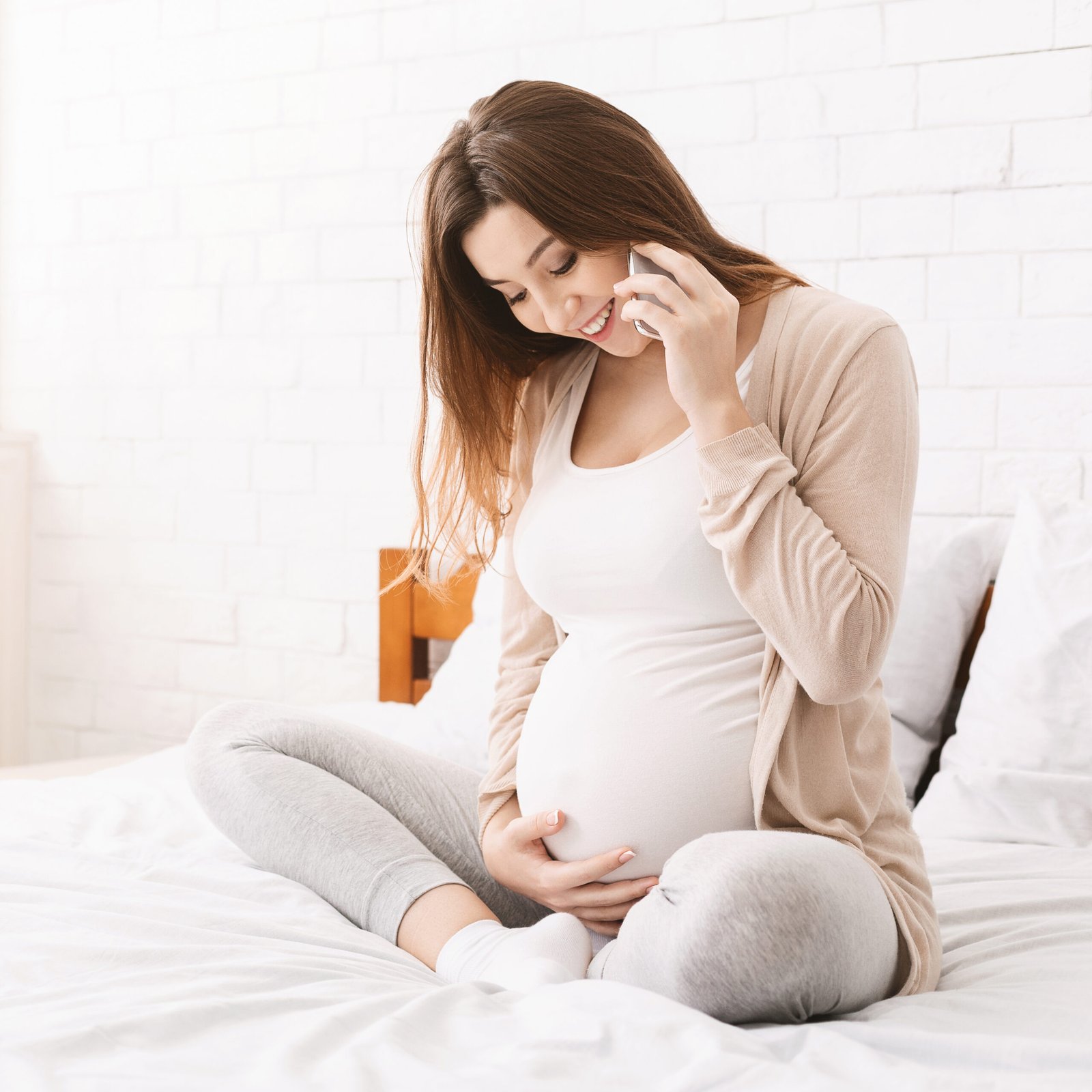 Cheerful pregnant woman talking on cellphone at home
